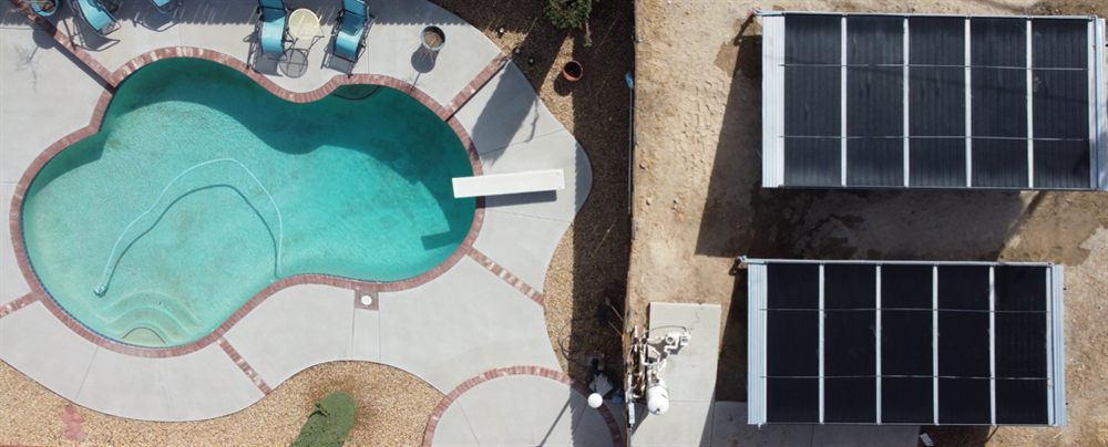 Overhead view of a pool with a diving board beside two ground-mounted solar collector arrays and the equipment pad between them