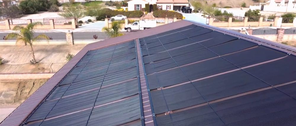 Aerial view of a tile hip roof fully covered with solar pool heating collectors, with a service truck in the driveway below
