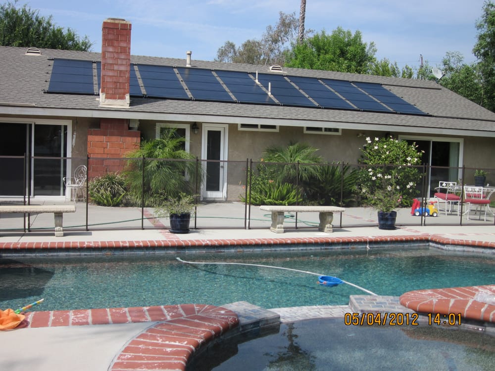 Rooftop solar collectors on a brick home above a backyard pool