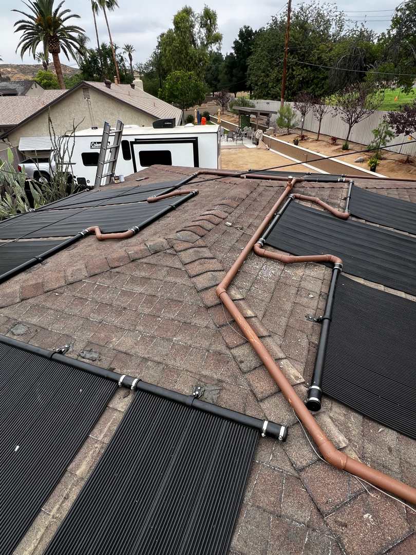 Copper header piping bridging a roof ridge to feed solar pool heating collectors on a shingle roof