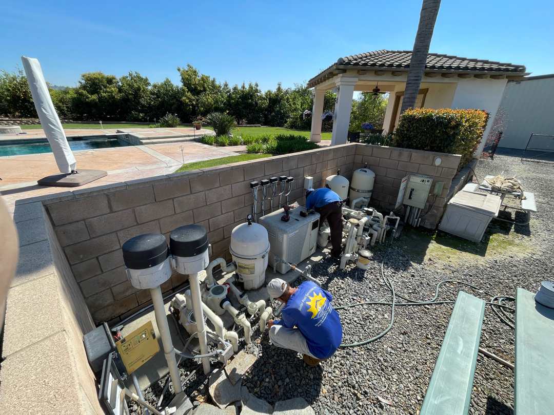 Two Solar Pool Services crew members in branded shirts working on a pool equipment pad