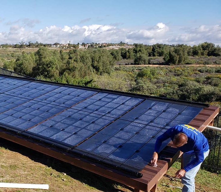 A crew member working on the frame of a large ground-mounted solar collector array above a green valley
