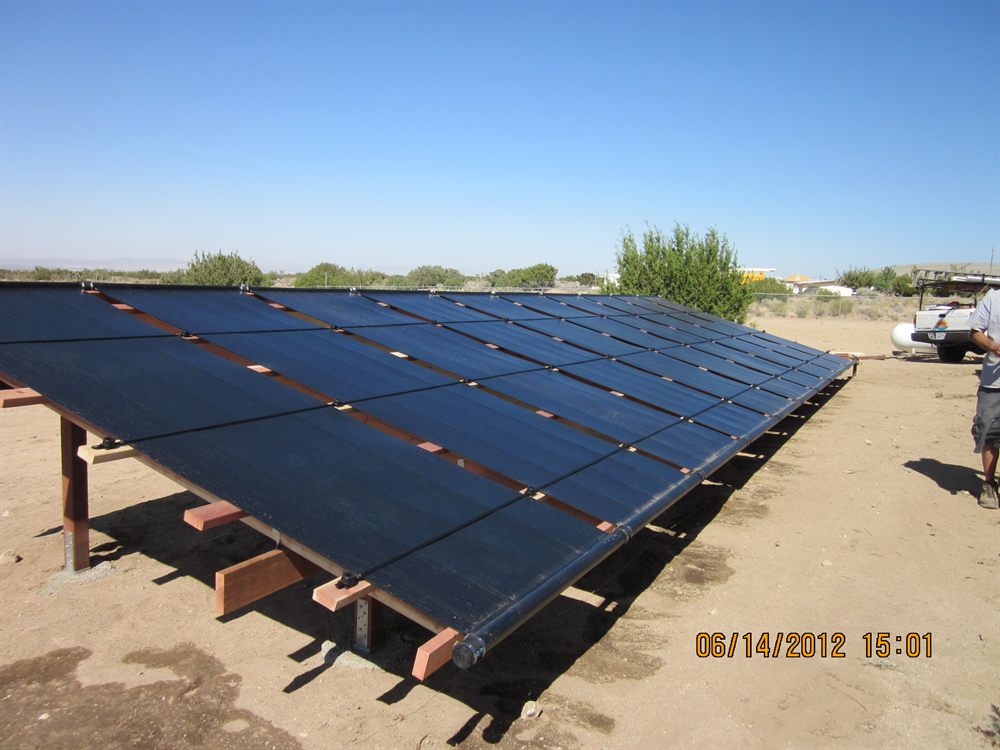 A large ground-mounted solar collector array on a timber rack in the high desert, with a service truck parked alongside