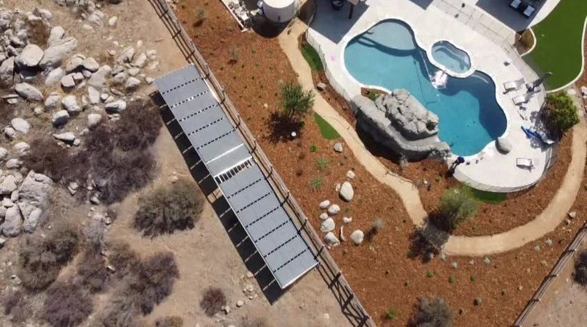 Aerial view of a desert backyard with a freeform pool and a long ground-mounted solar collector rack along the fence line