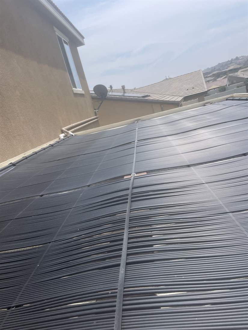 A large solar pool heating collector array across a low-slope roof beside a two-story home