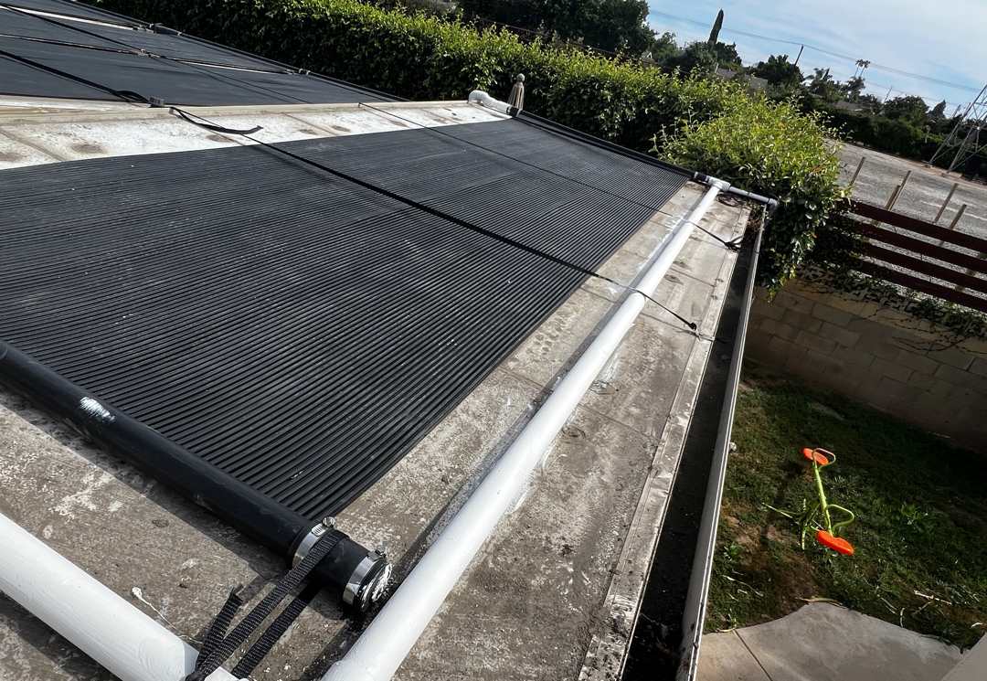 Black solar pool heating collectors on a flat low-slope roof with white PVC supply and return headers