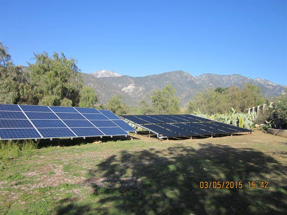 Ground-mounted solar pool heating collectors beside a photovoltaic array, with snow-dusted foothills behind