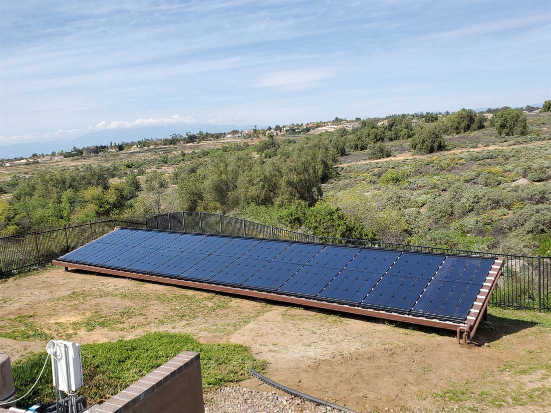 A ground-mounted solar pool heating collector array on a low rack overlooking foothills and distant snow-capped mountains