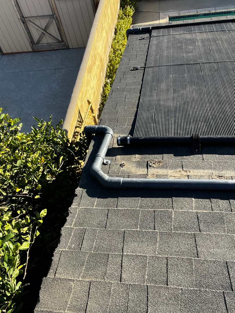 Close-up of gray PVC header plumbing with union couplers running from a solar collector across a shingle roof