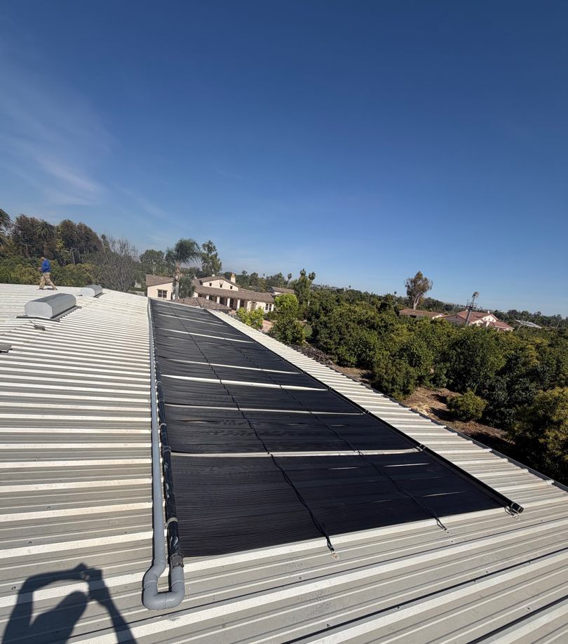 Solar pool heating collectors mounted on a white metal roof at a grove estate, with a crew member at the ridge