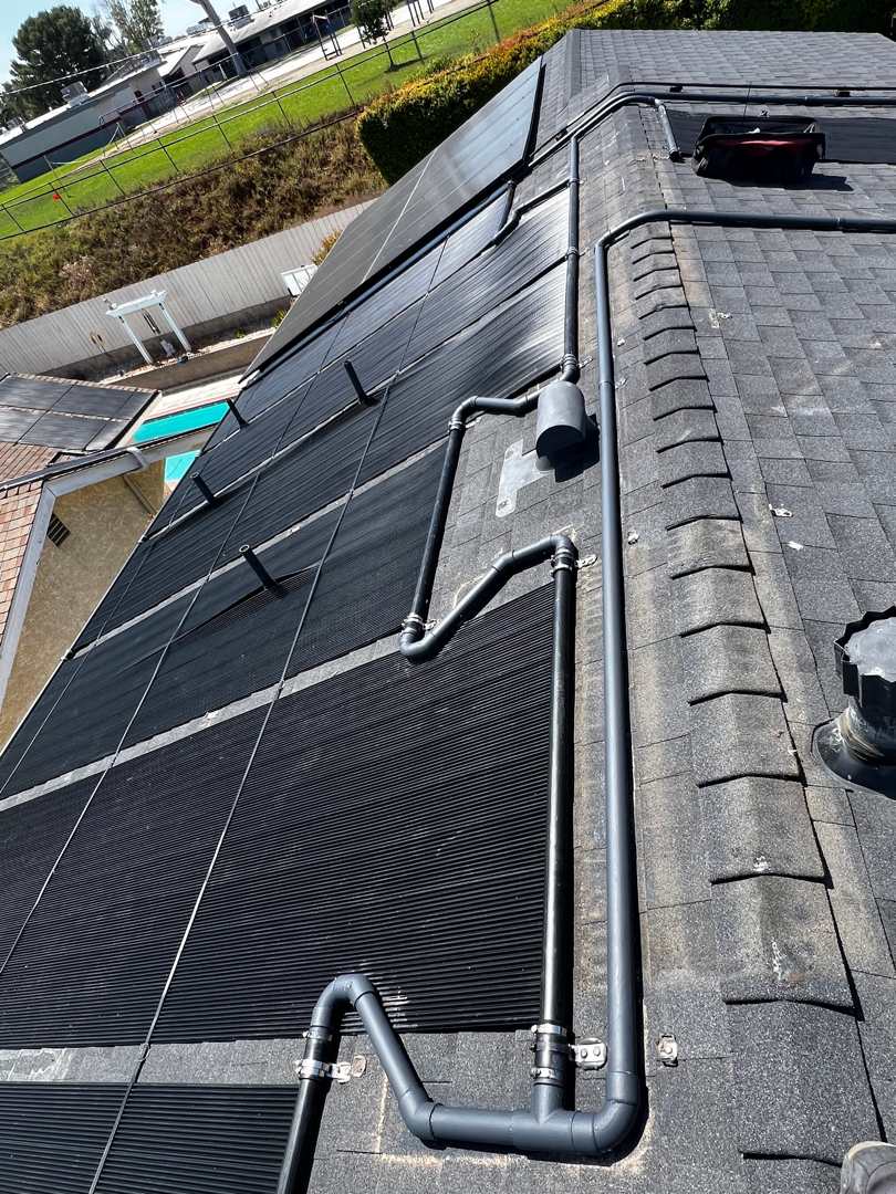 A gray PVC plumbing riser and roof run feeding solar pool heating collectors above a pool and spa