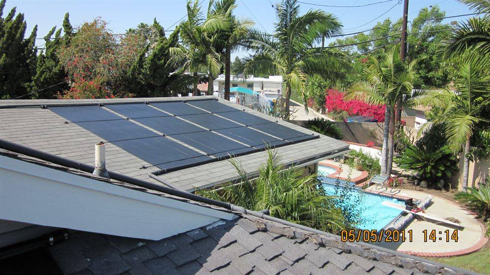 Solar pool heating collectors on a shingle roof above a backyard pool and raised spa