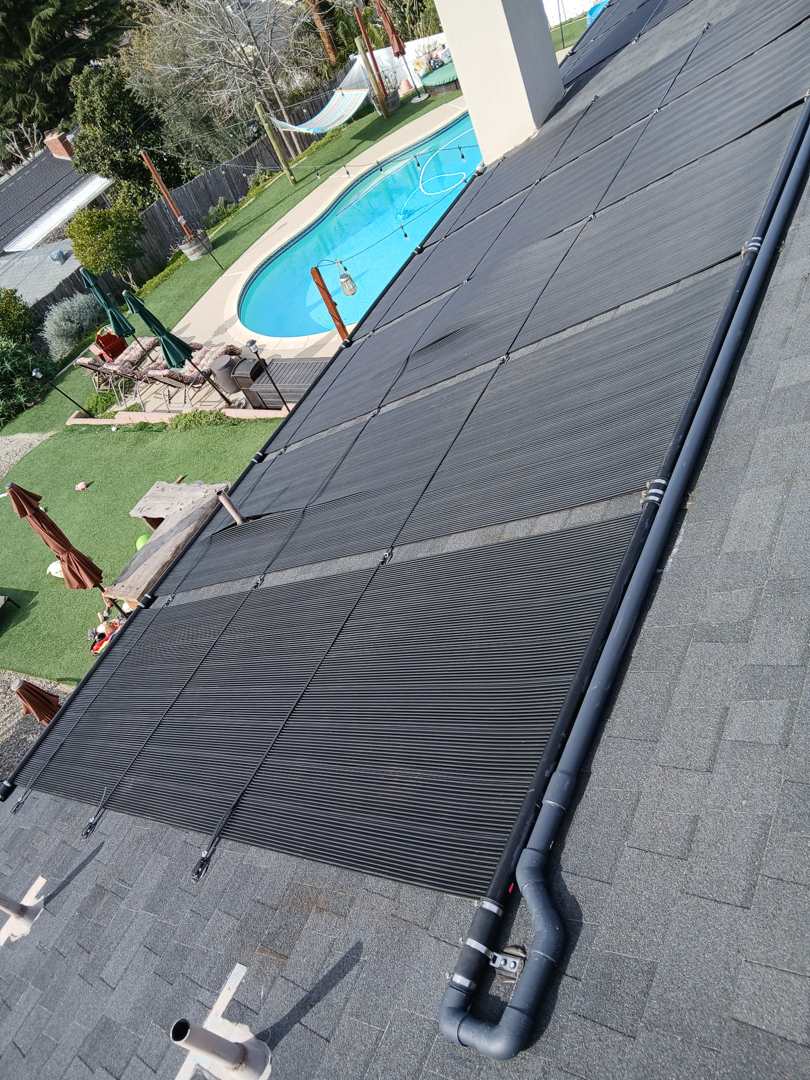 A large solar pool heating array on a shingle roof above a curved backyard pool