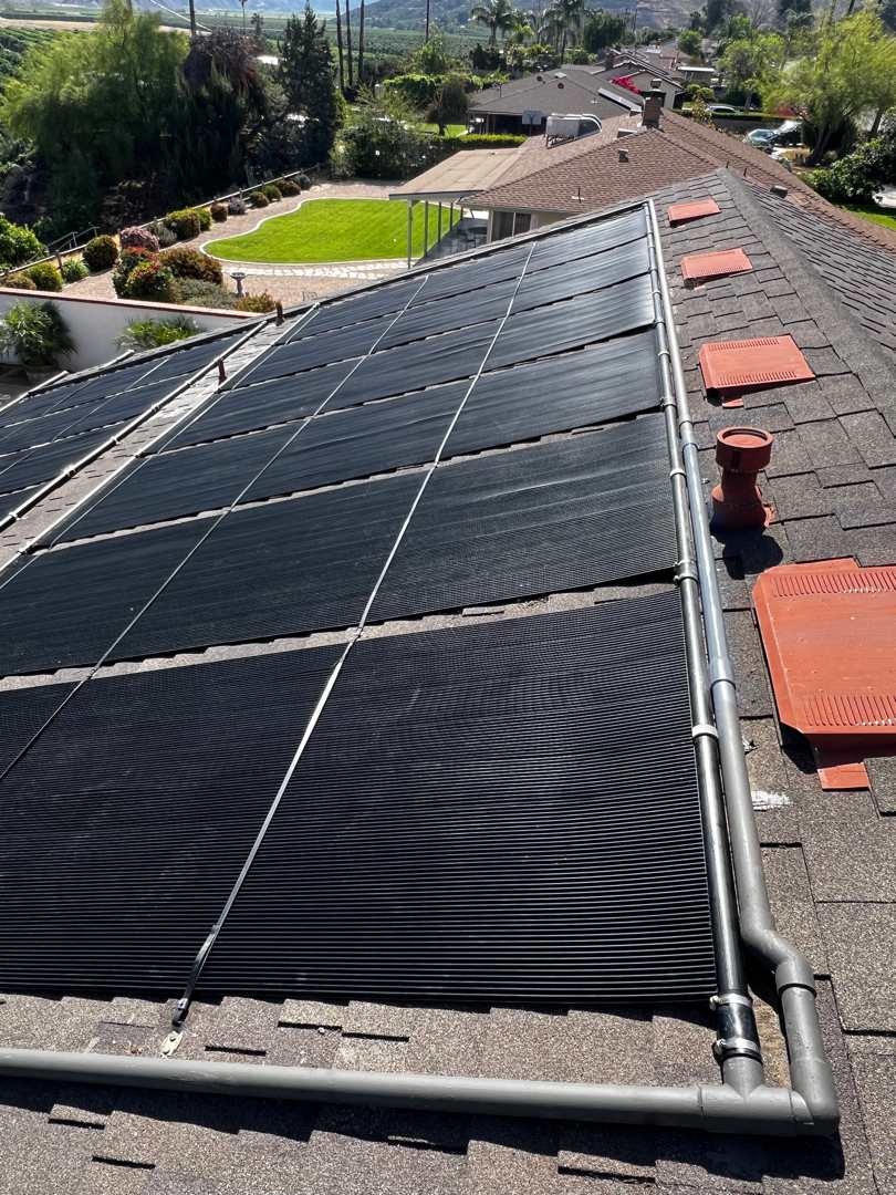 A full solar pool heating array on a brown shingle roof overlooking agricultural hills