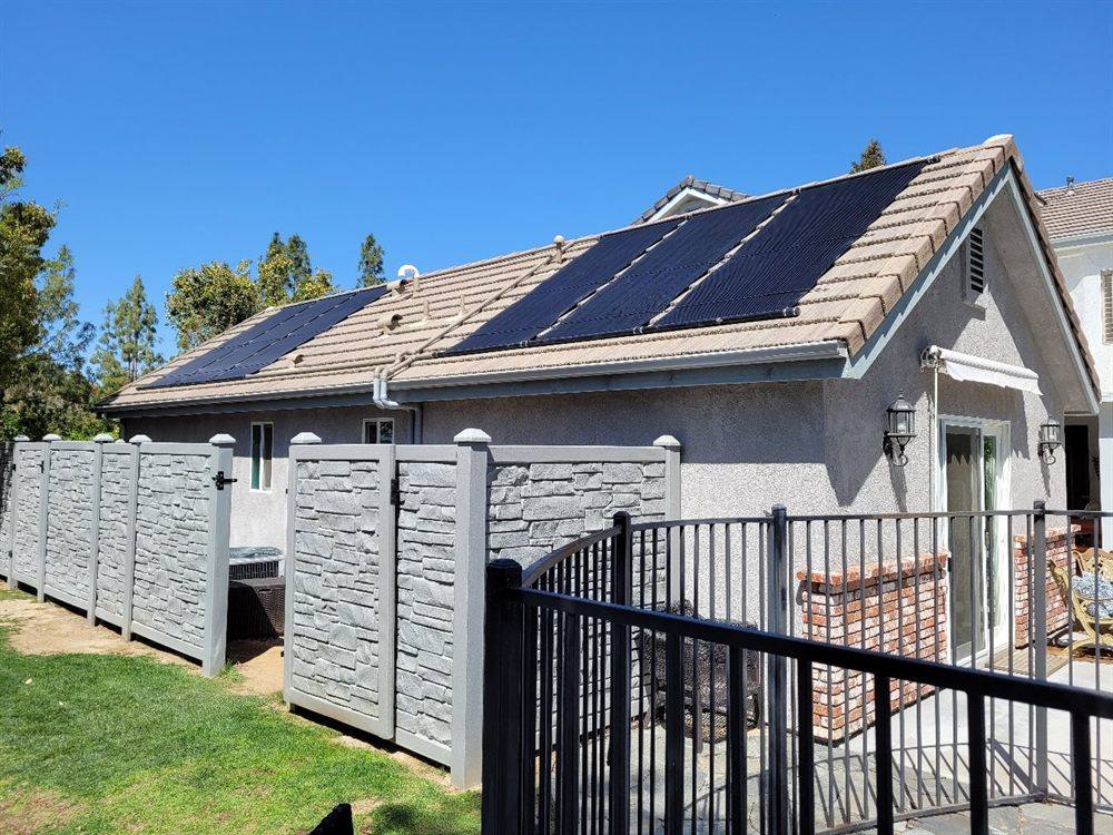 Four solar pool heating collectors on a tan tile roof with plumbing running down toward the gutter