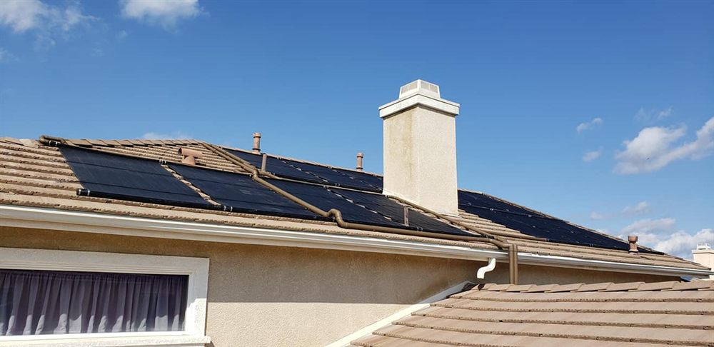A finished run of solar pool heating collectors on a tile roof with the header piping painted to match