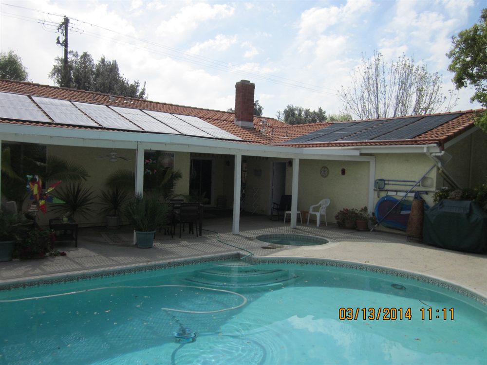 A pool and round spa below a barrel tile roof carrying solar pool heating collectors and photovoltaic panels