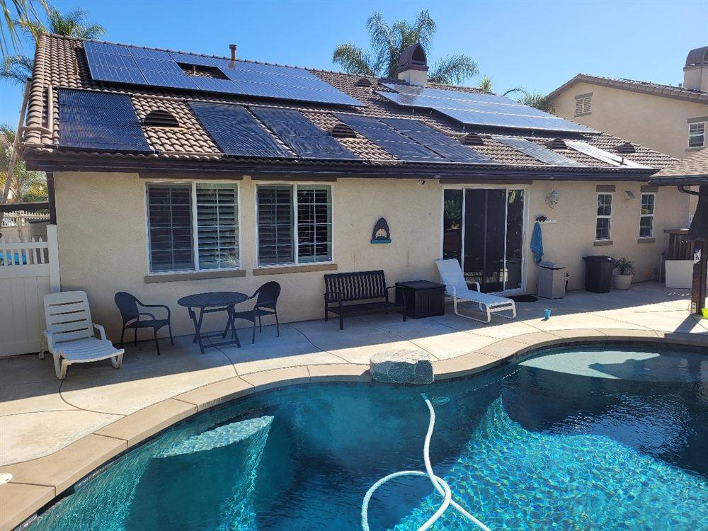A kidney-shaped pool below a tile roof carrying both solar pool heating collectors and photovoltaic panels